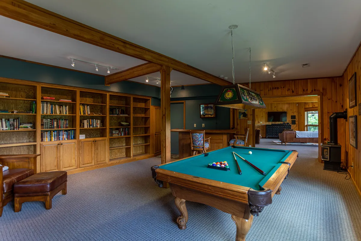 This image features a stylish game room with a pool table as its centerpiece, flanked by bookshelves and a comfortable seating area. The space exudes a cozy, social atmosphere ideal for friendly competition and leisure activities.