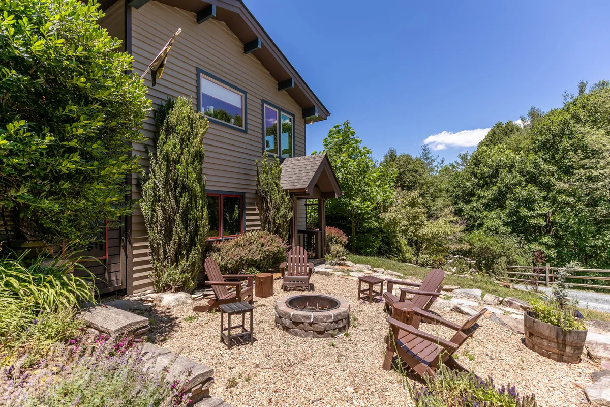 This image showcases a cozy fire pit area surrounded by Adirondack chairs and a landscaped garden, set against a backdrop of natural greenery. The space is inviting, perfect for evening gatherings or storytelling under the stars, and conveys a sense of family togetherness and outdoor enjoyment.