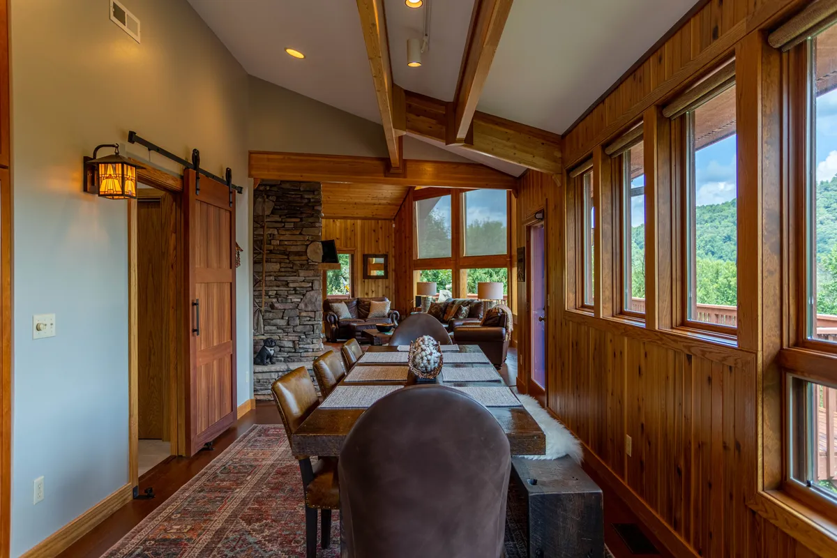 A welcoming dining area with a large table set for family meals, positioned next to a stone fireplace and expansive windows showcasing breathtaking mountain views. The space is bathed in natural light, creating a cozy yet vibrant atmosphere.