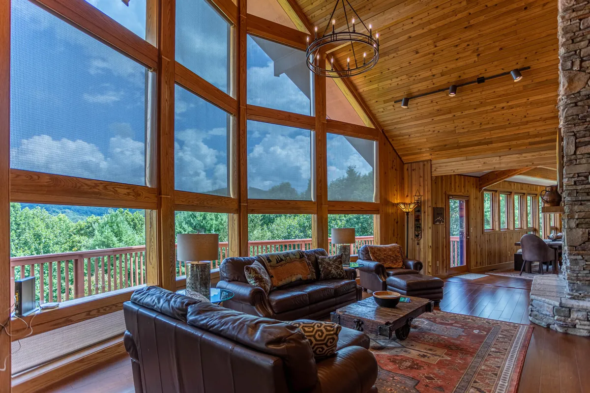A spacious living area with large windows that capture mountain views, a rustic stone fireplace, and a cozy seating area under wooden beams. The natural light and inviting decor create a perfect environment for gathering and relaxation.