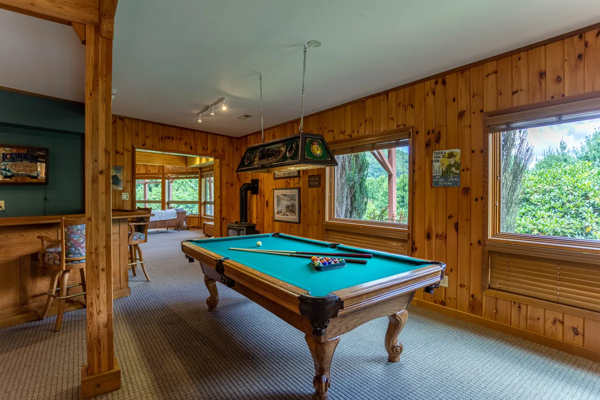 This image spotlights the heart of the game room, featuring a classic pool table set against rich wooden paneling. Sunlight streams in through the windows, illuminating the space and adding to the inviting, casual vibe perfect for friendly competition or relaxed hangouts.