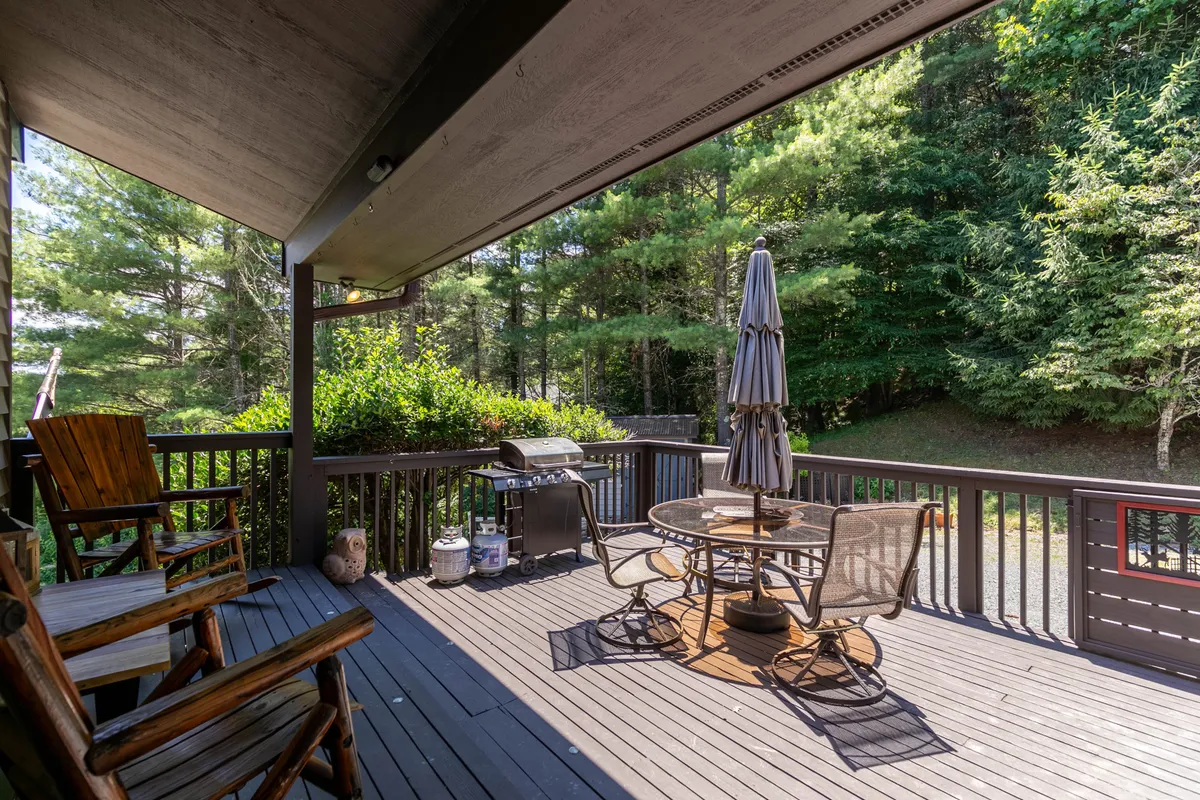 A welcoming outdoor dining area features a barbecue grill, umbrella-shaded table, and rocking chairs, all overlooking a green, peaceful landscape. The space is ideal for socializing and outdoor meals after a day of play or exploration.