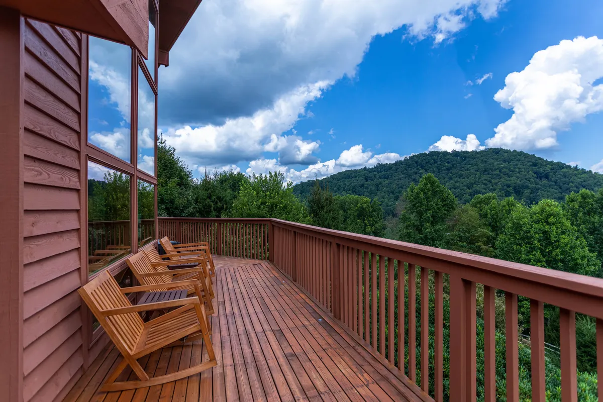 A wooden deck overlooking rolling hills and majestic mountains under a wide sky. The deck offers a tranquil vantage point with space for outdoor relaxation, making it ideal for savoring the scenery or enjoying an alfresco barbecue.