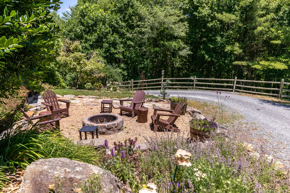 Set outdoors, this image features a fire pit surrounded by Adirondack chairs amidst flowering plants and a stone pathway. The scene invites guests to gather for storytelling, s’mores, or stargazing, just steps from the game room.