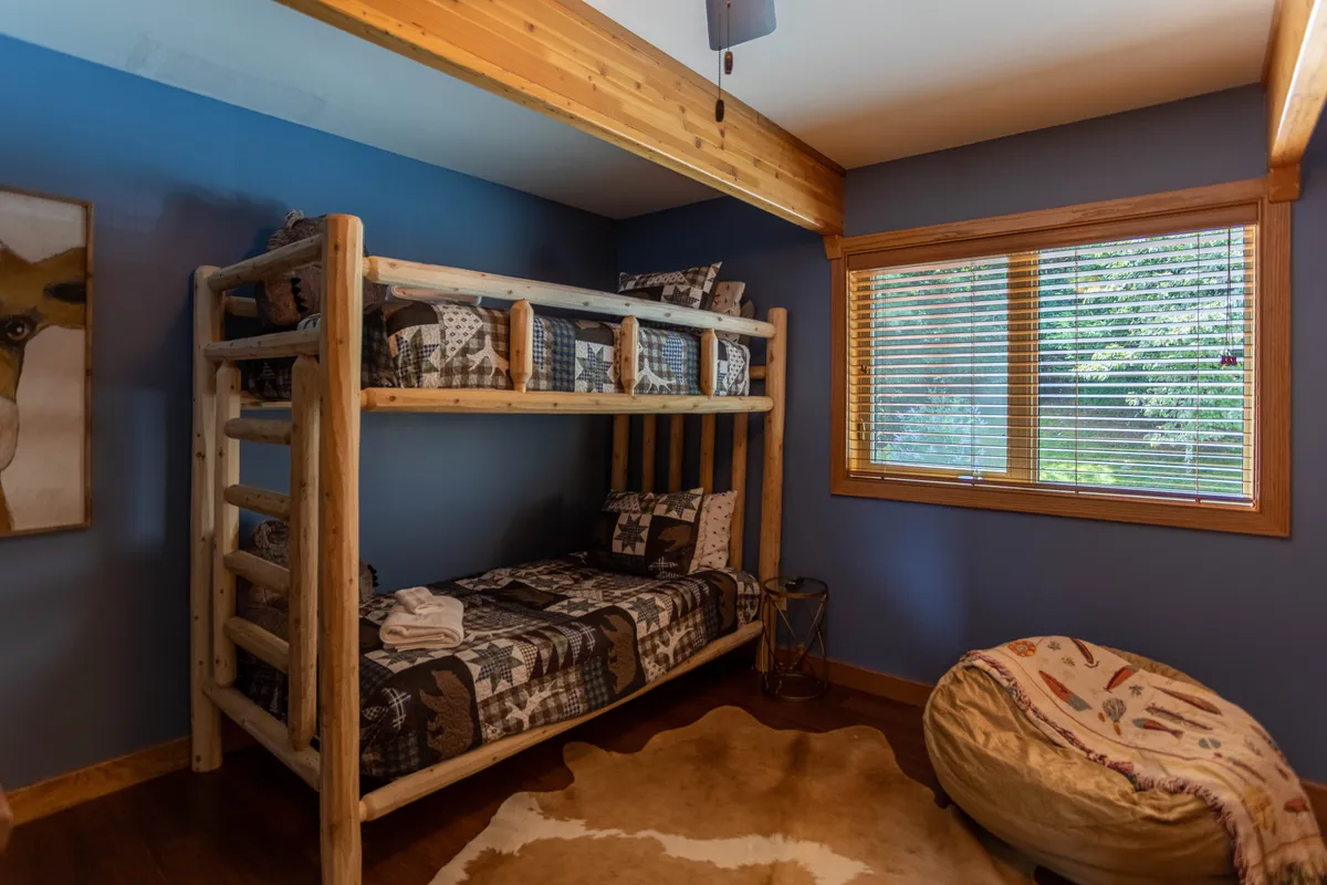 A playful bunk room featuring a bunk bed, a cowhide rug, a bean bag chair, and a window letting in natural light. The space is relaxed and casual, designed for group activities like playing games, reading, or lounging with friends.