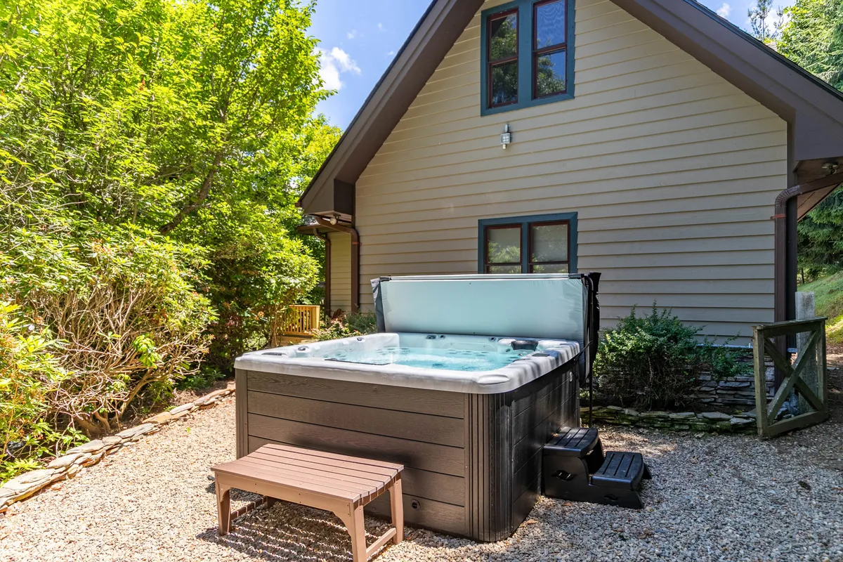 A close-up view of the hot tub nestled in the yard, surrounded by greenery and adjacent to the house exterior. The inviting bubbling water, plus the lush landscaping and privacy, combine to evoke relaxation. The scene is tranquil, perfect for enjoying a soak after outdoor adventures.