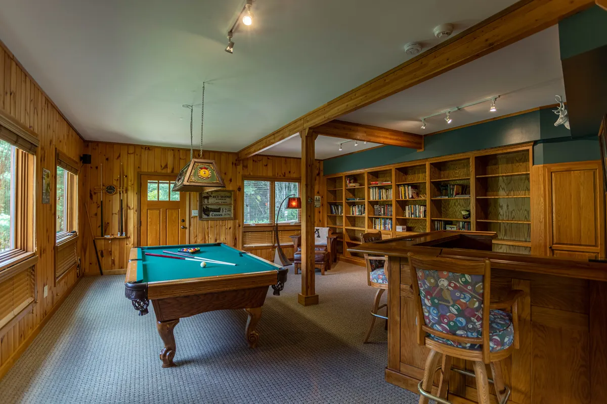 This image presents a broader view of the entertainment area, including the pool table, a cozy seating area, bookshelves, and a bar. The scene conveys the versatility of the game room as a place for billiards, socializing, and relaxed downtime, echoing the multi-purpose nature described in the section.