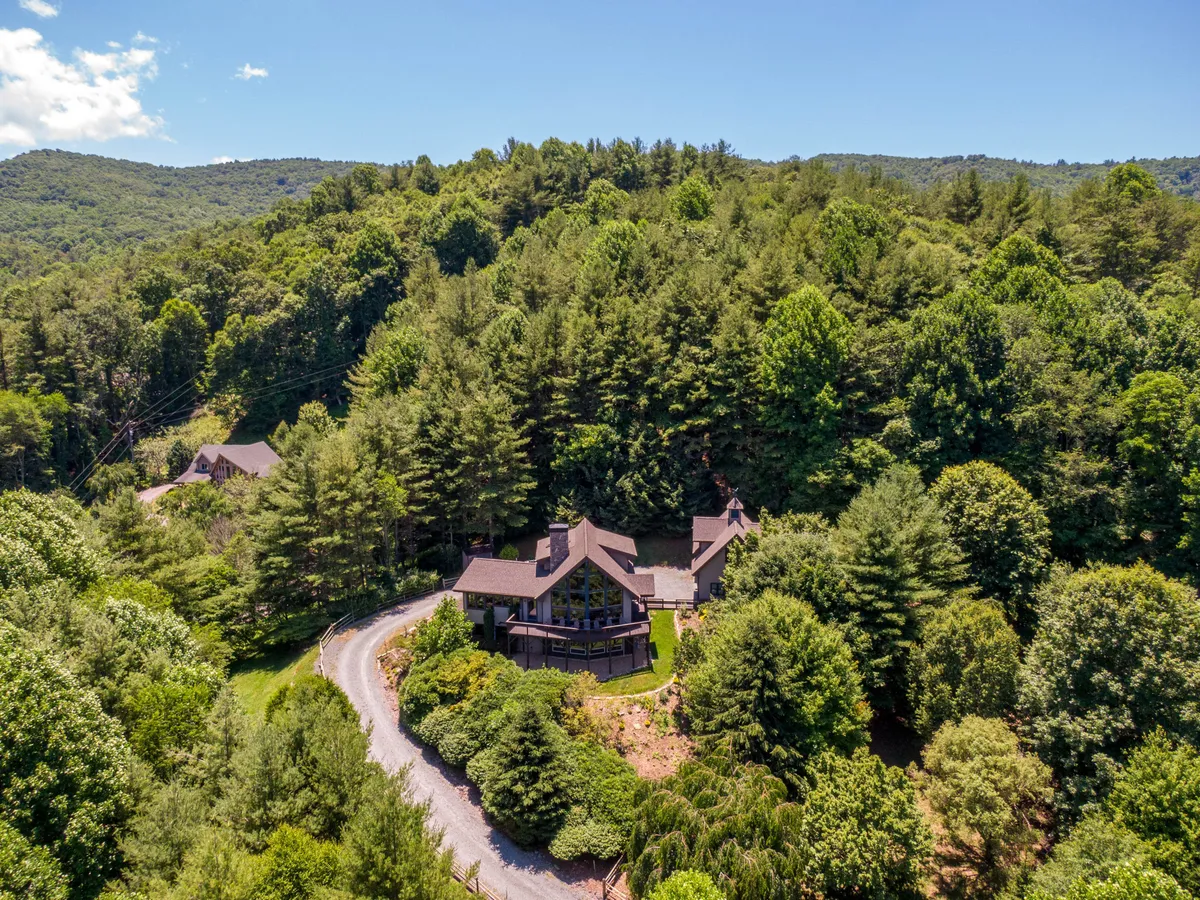 A wide exterior shot of the house, set amid a winding driveway and surrounded by mature trees. The open landscape gives a sense of the property's generous acreage, ideal for outdoor adventures with pets.