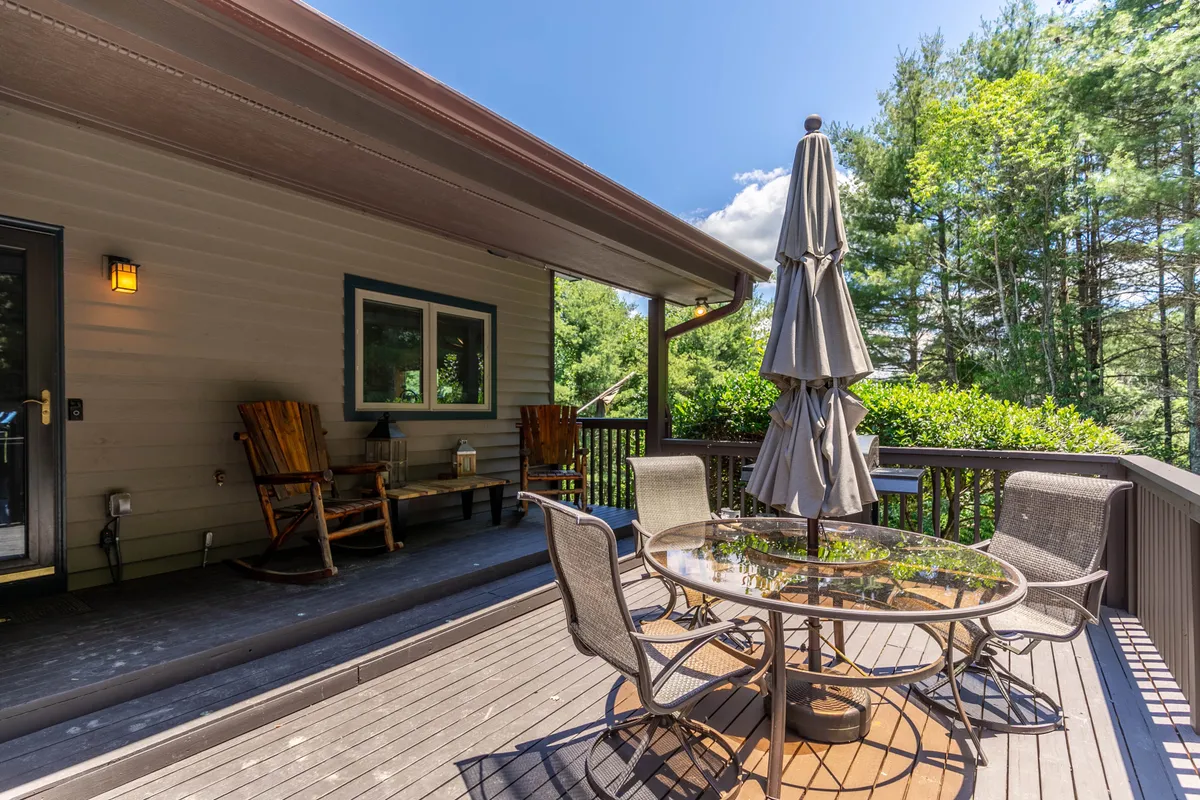 An outdoor dining area featuring a round table under a large umbrella, with rocking chairs and verdant greenery all around. The setup is perfect for shared meals, sunset dinners, and stargazing nights, fostering group connection in a scenic environment.