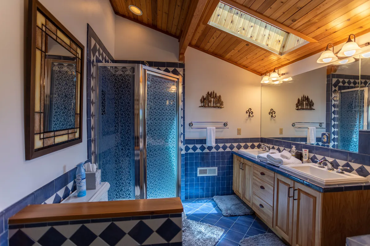 A serene bathroom with a double sink, walk-in shower, wooden ceiling, and large mirrors. The space feels spa-like and inviting, perfect for unwinding after a busy day.