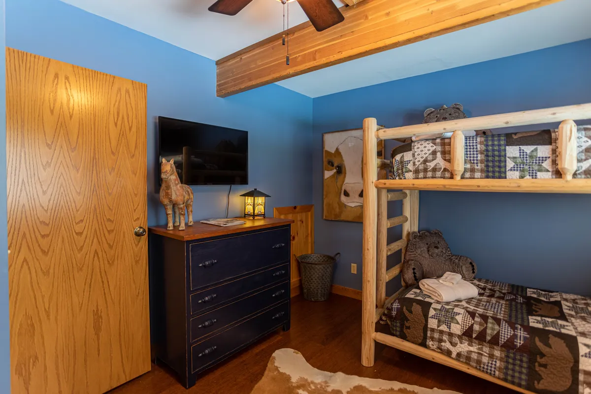 A playful and warm bunk room featuring a bunk bed, dresser, artwork of a cow, TV, and a lantern. The room is designed for both fun and relaxation, suitable for children or young-at-heart guests.